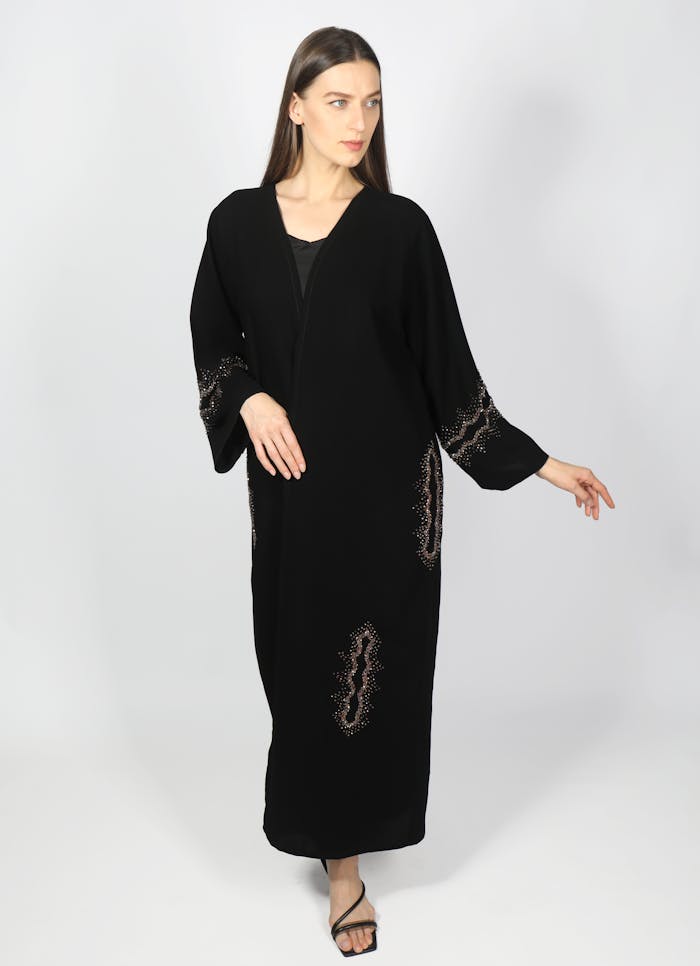 Stylish woman wearing a black abaya posing elegantly against a white background.