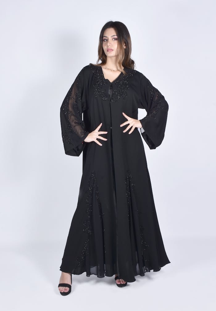 Full-length portrait of a woman in a black abaya with embroidery, striking a pose in a studio setting.
