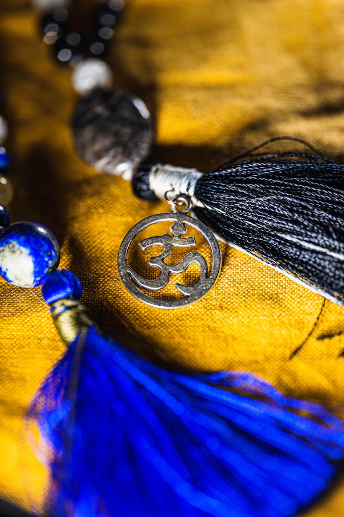 gallery-3 Detailed view of Om symbol pendant with blue and black tassels on vibrant fabric.