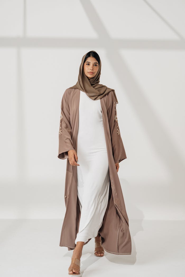Portrait of a woman in a brown abaya and hijab, elegantly posed indoors.