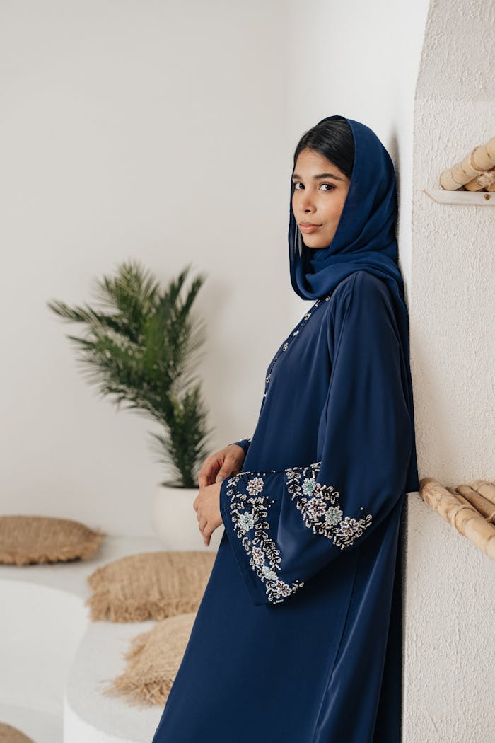Elegant woman in a blue embroidered abaya, posing indoors with a serene expression.