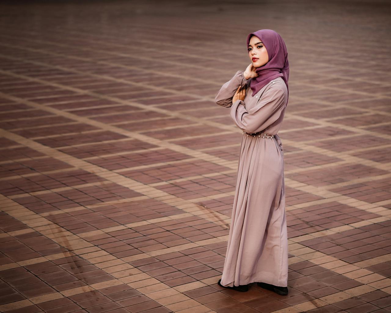 Stylish woman wearing a pink hijab and flowing dress on a geometric tiled floor, exuding grace and elegance.