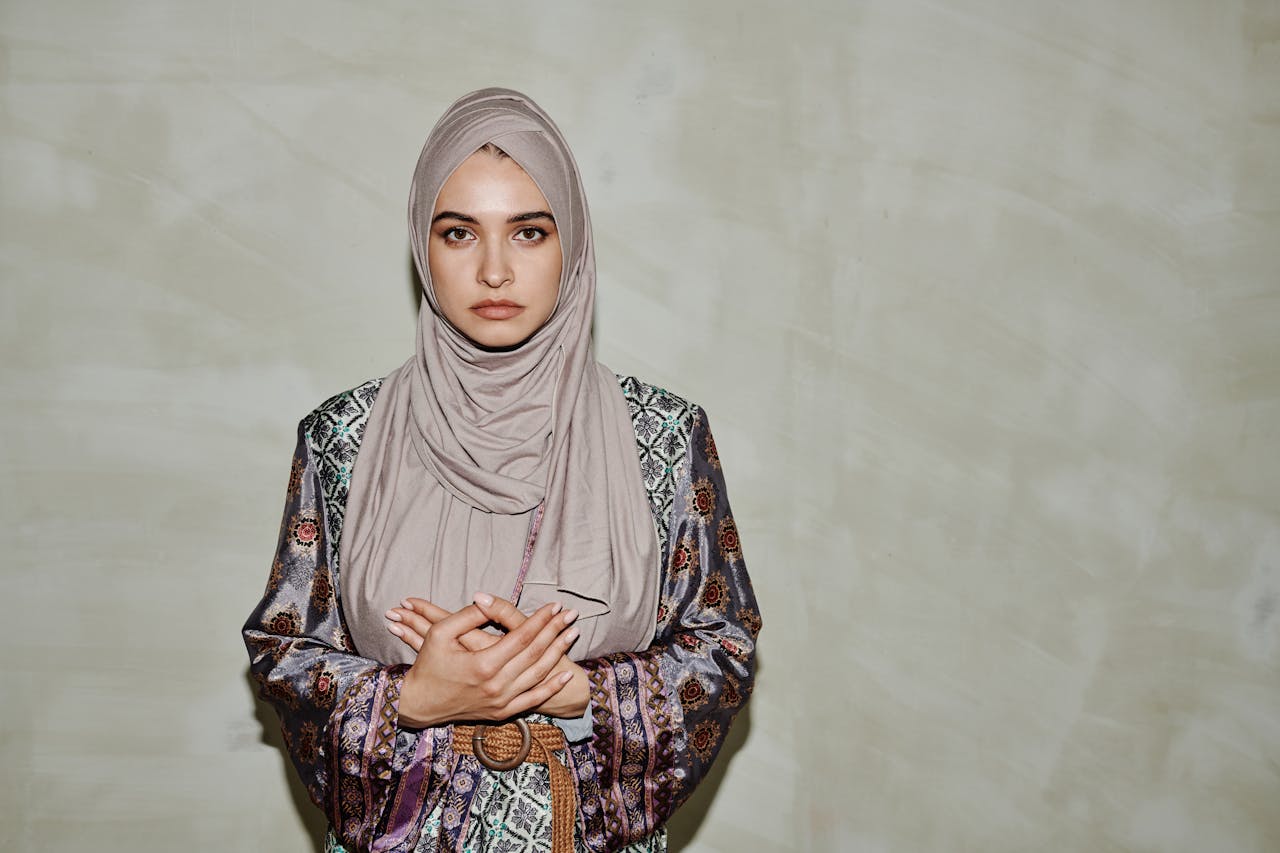 Elegant portrait of a Muslim woman wearing a hijab and patterned dress, looking serious.