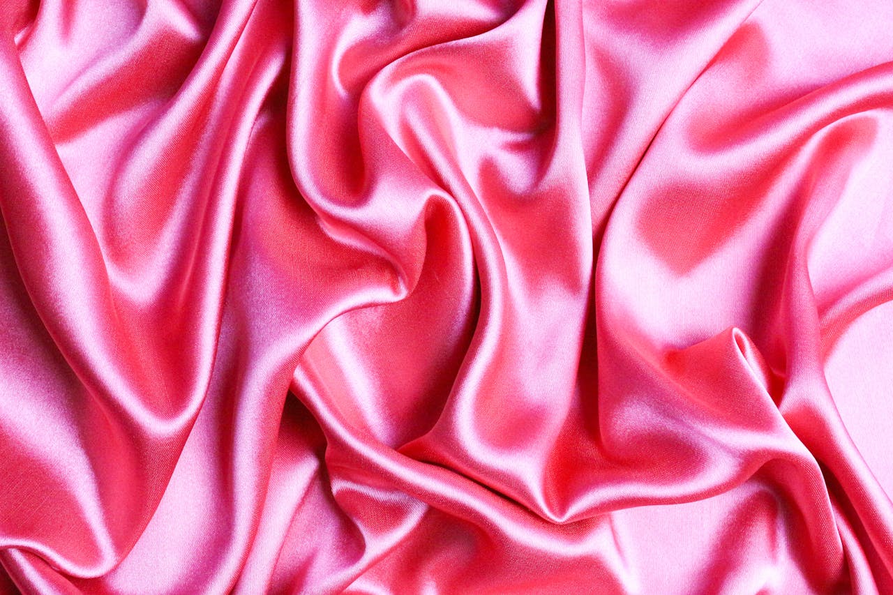 Close-up view of smooth pink silk fabric with elegant creases and drapery.